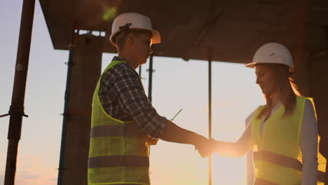 Building-teamwork-partnership-gesture-and-people-concept---close-up-of-builders-hands-in-gloves-greeting-each-other-with-handshake-on-construction-site